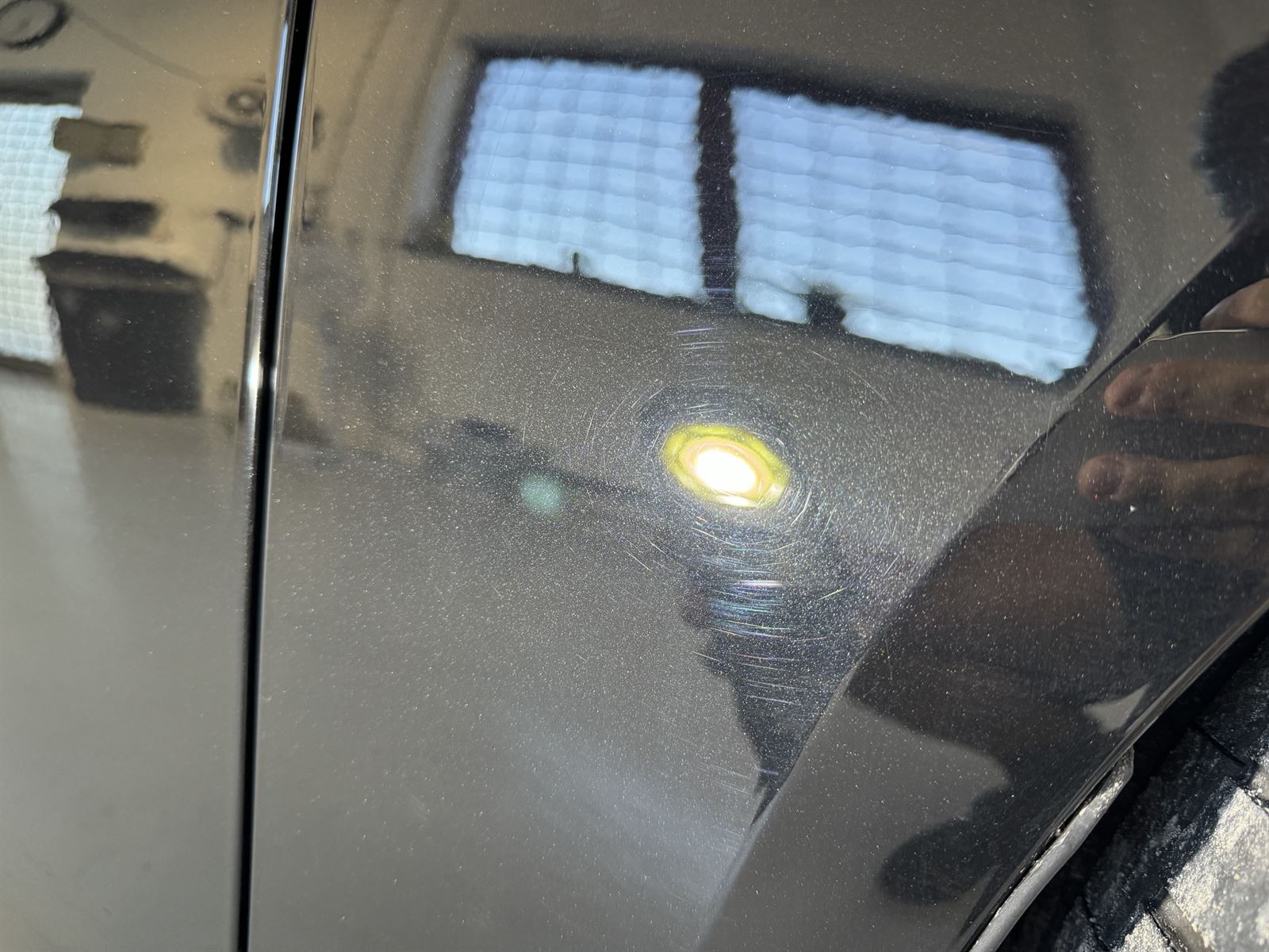 Sort bildør med cirkulære vaskeridser, der ses i lyset fra en lampe, før polering